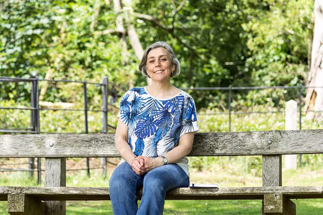 Mands sitting on a bench in a park, writing